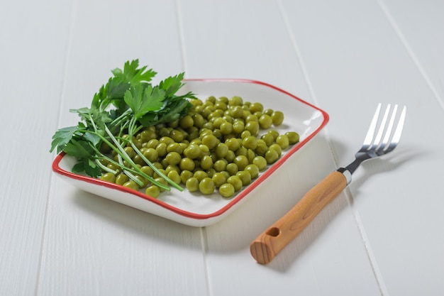 A fork and a plate of canned peas on a white wooden table. Dietary vegetarian food.