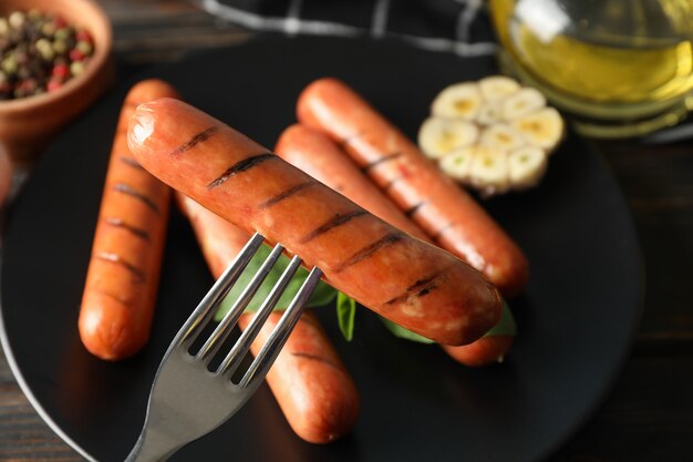 Fork and plate with sausage on wooden, close up