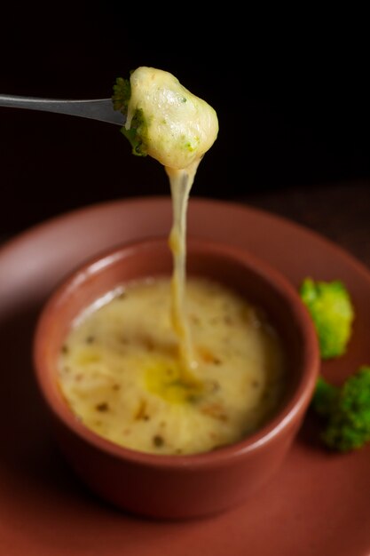 Photo fork with broccoli dipped in melted cheese bowl