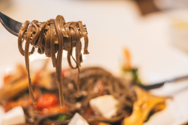 Fork with buckwheat noodles, on background of blurred plate with a vegan dish