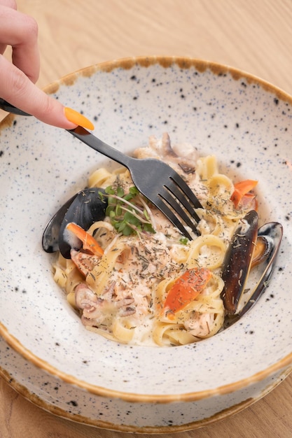 Fork in womans hand with seafood pasta under delicate cream sauce