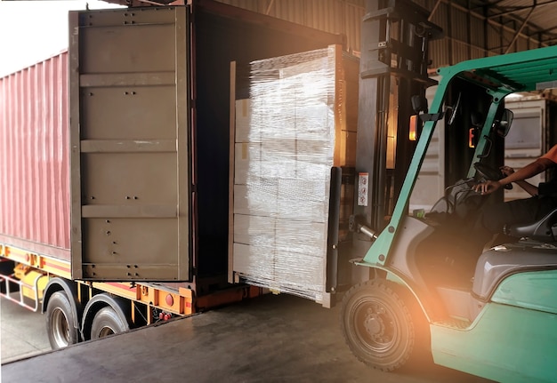 Forklift driver loading heavy cargo pallet into shipping container truck.