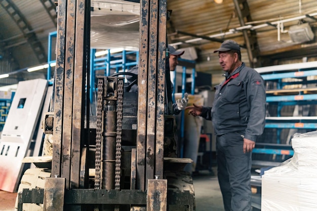 Forklift driver and worker in an industrial warehouse in the foreground the mechanism of the loader