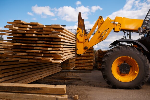 Forklift loads the boards in the lumber yard outdoor. Autoloader works on timber mill warehouse, woodworking industry, carpentry. Wood processing on factory, forest sawing, sawmill