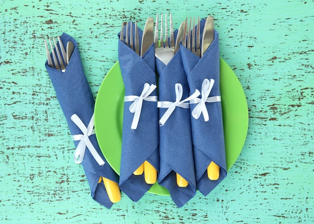 Foto forchette e coltelli avvolti in tovaglioli di carta blu su uno sfondo di legno colorato