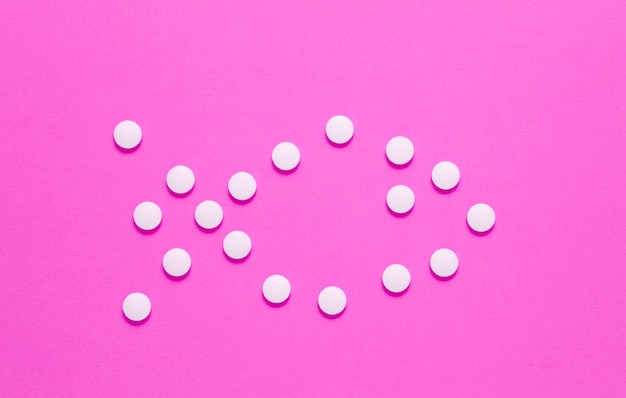 Form of fish laid out of white pills on pink background. Medical minimalistic concept, top view