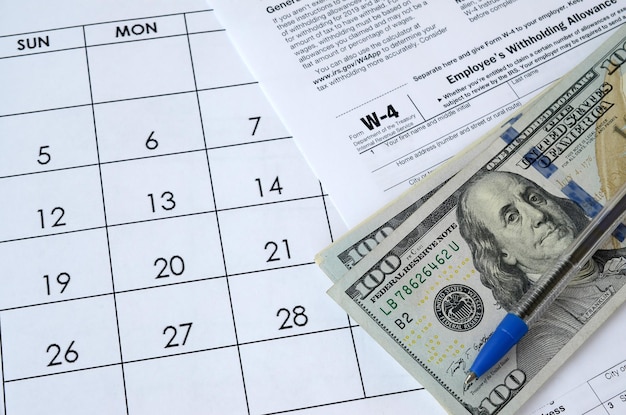 フォーム W4 従業員の源泉徴収手当証明書と青色のペンとドル札がオフィス カレンダーにある 内国歳入庁税フォーム