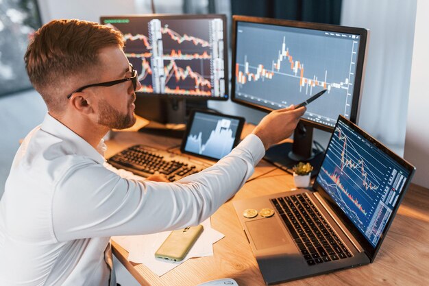 In formal clothes Young businessman is in office with multiple screens