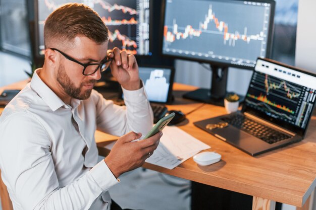 In formal clothes Young businessman is in office with multiple screens