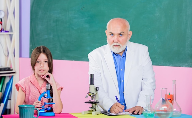 Формула маленькая девочка с мужчиной-репетитором изучает химию наука в классе использует увеличительное стекло микроскопия лабораторное оборудование зрелый учитель биологии ученица в школьной лаборатории