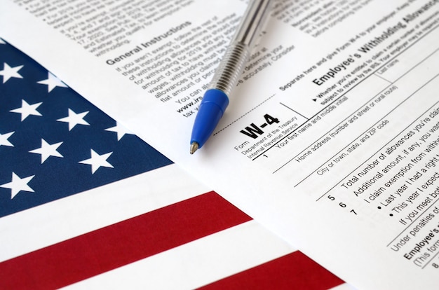 Formulier W-4 werknemer inhoudingsbewijs en blauwe pen op vlag van Verenigde Staten. Belastingformulier voor interne inkomsten