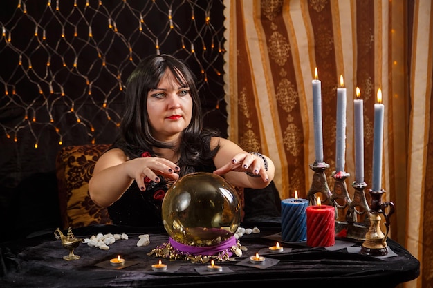 Брюнетка-гадалка в волшебном салоне читает будущее в хрустальном шаре и делает движения руками