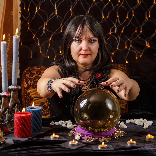 Fortune teller woman brunette in a magic salon reads the future in a crystal ball