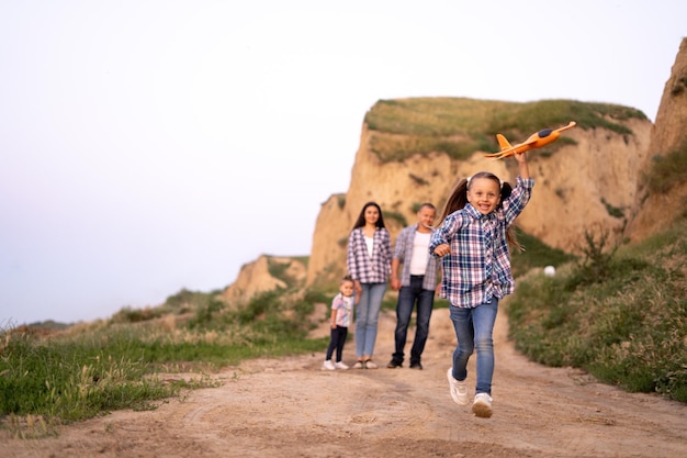 Foster family dad and mom with two daughters walking at sunset along a cliff or rocks in the summer evening child launching airplane happy parents and kids girls Family adoption concept