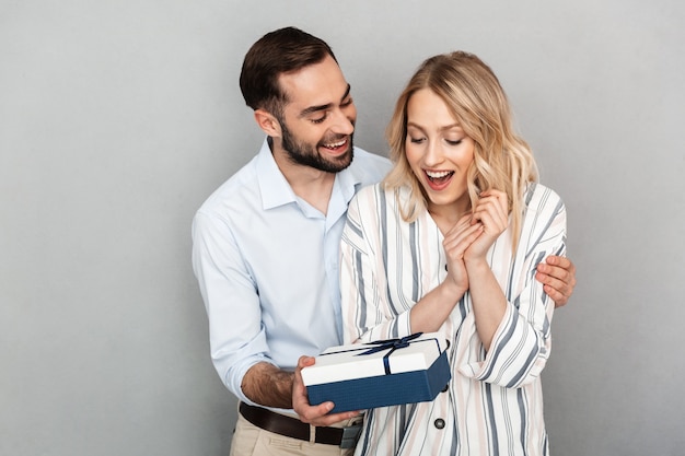 Foto close-up van brunette man in casual kleding glimlachend en cadeau geven aan zijn vriendin geïsoleerd over grijze muur