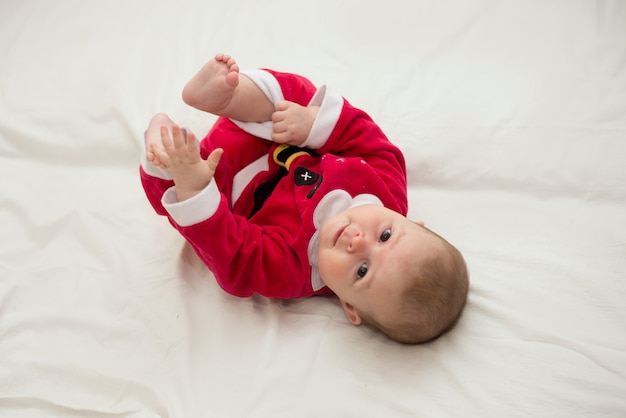 Foto die van baby op zijn rug ligt die het kostuum van de Kerstman over laken draagt