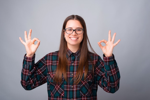 Foto die van jonge vrouw ok gebaar over witte muur toont