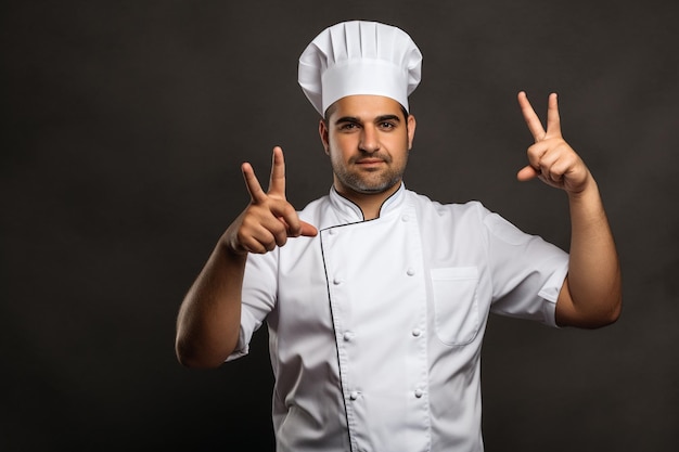 Foto mannelijke chef-kok in wit uniform die een lekker teken maakt op een grijze achtergrond