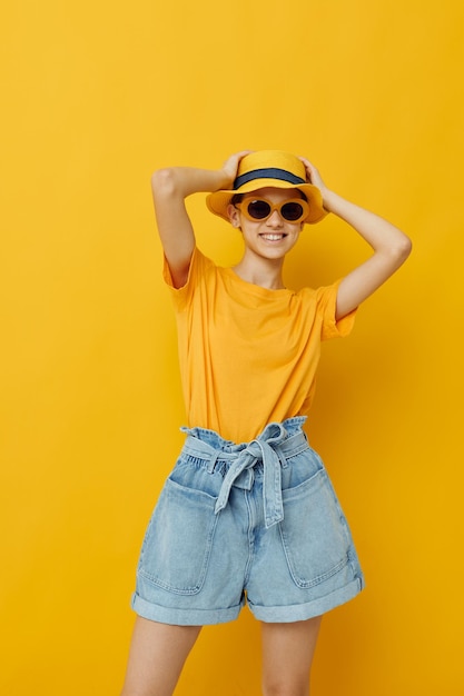 Foto mooi meisje in zonnebril een gele t-shirt en hoed zomer stijl gele achtergrond