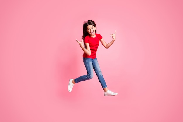 Foto op volledige grootte van het gekke meisje springshow gehoornde symbool draagt rood t-shirt denim geïsoleerd over pastelkleurige achtergrond