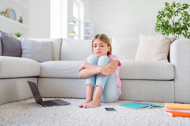 Foto op volledige grootte van quarantaine kind meisje basisschool student moet thuis blijven gefrustreerde emotie juffrouw klasgenoten zitten vloertapijt in huis binnenshuis