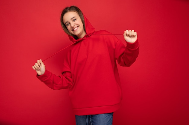Foto-opname van een aantrekkelijk positief, gelukkig lachend brunette meisje met een trendy rode hoodie
