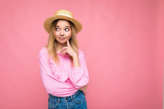 Foto-opname van een jonge, mooie, doordachte blonde vrouw met een stijlvolle roze crop top en stro