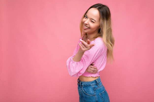 Foto-opname van een jonge, mooie, schattige, gelukkige blonde vrouw die een stijlvolle roze crop-top draagt, geïsoleerd over