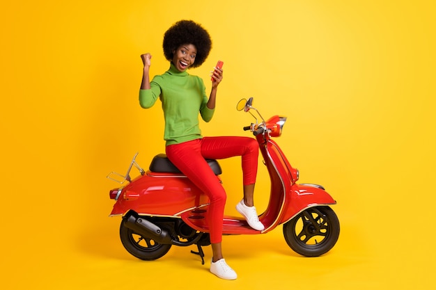Foto portret van jonge brunette afro-amerikaanse fietser op rode fiets met mobiele telefoon ontvangen winnende sms-bericht dragen casual outfit geïsoleerd op levendige geel gekleurde achtergrond