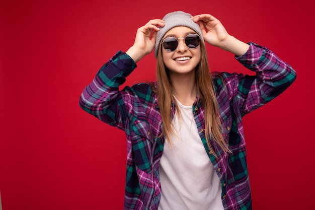 Foto schot van mooie positieve jonge brunette vrouw dragen zomer casual kleding en stijlvolle zonnebril geïsoleerd over kleurrijke achtergrond muur camera kijken.