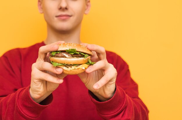 Foto sluiten. De mens houdt in zijn handen een heerlijke grote hamburger op geel.