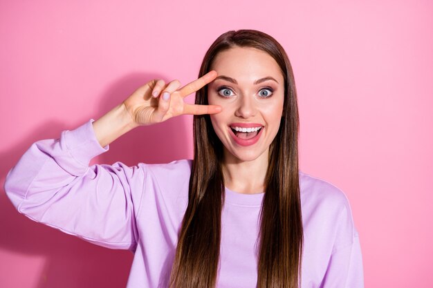 Foto van aantrekkelijke coole vrolijke dame met twee vingers v-teken symbool in de buurt van oog zeg hallo vrienden vergadering partij verzamelen dragen casual paarse trui geïsoleerde roze pastel kleur achtergrond