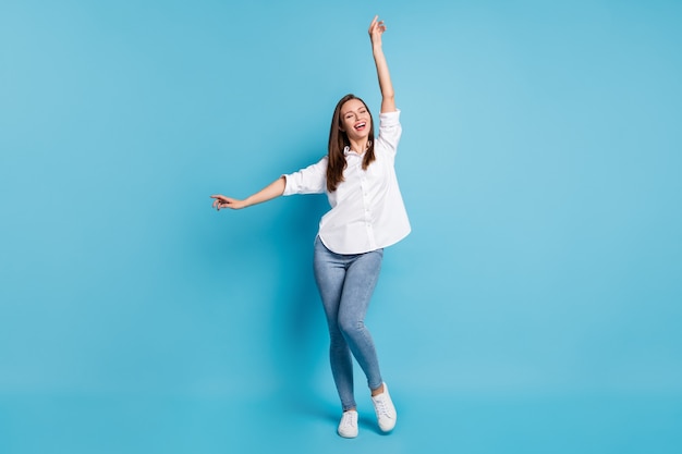 Foto van aantrekkelijke grappige dame die dansen draagt wit overhemd jeans sneakers geïsoleerde blauwe kleur achtergrond