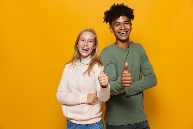 Foto van Afro-Amerikaanse man en blanke vrouw 16-18 met beugels gebaren op camera, geïsoleerd op gele achtergrond