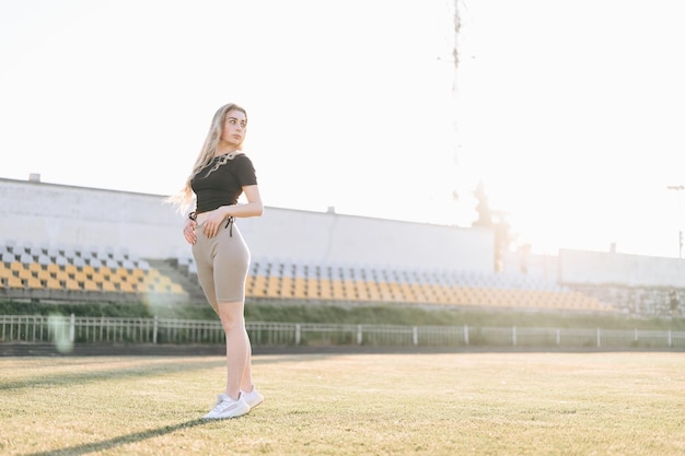 Foto van atletisch meisje in stadion met groothoek vanaf onderkant Gezonde vrouw kijkt weg in zonnestralen