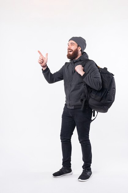 Foto van bebaarde hipster man met rugzak en wijst weg op de hoek