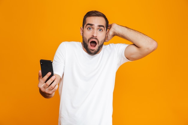 Foto van blanke man 30s in vrijetijdskleding met smartphone, geïsoleerd