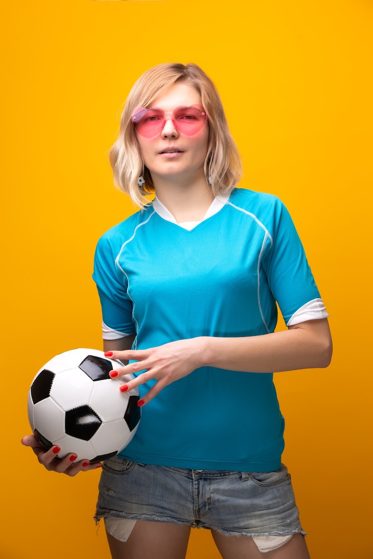 Foto foto van blonde in roze bril met voetbal op oranje backgroundin studio