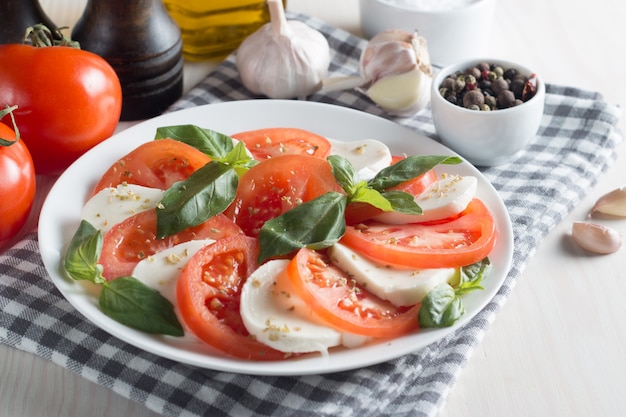 Foto van Caprese-Salade met tomaten, basilicum, mozarella, olijven en olijfolie op houten achtergrond. Italiaanse traditionele caprese saladeingrediënten. Mediterraan, biologisch en natuurvoedingconcept.