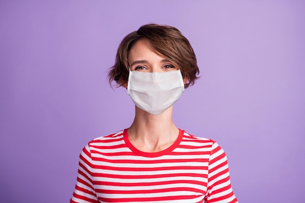 Foto van charmant jong meisje kijkt camera draagt medisch masker gestreept t-shirt geïsoleerde violette kleur achtergrond