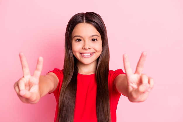 Foto van charmant latijns-meisje dat v-teken rood t-shirt draagt dat over roze kleurenachtergrond wordt geïsoleerd