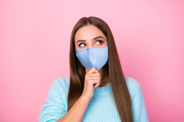 Foto van dame dromer opzoeken lege ruimte hand op kin draag masker gebreide blauwe trui geïsoleerde pastel roze kleur achtergrond