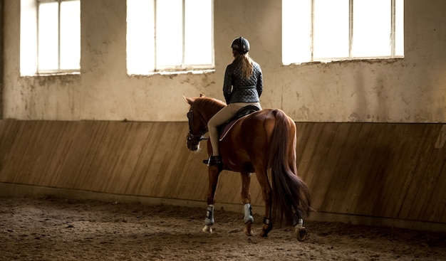 Foto van de achterkant van een vrouw die paardrijden in manege