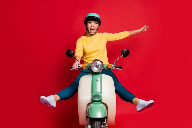 Foto van de gekke onbezorgde rit van het bromfietsbestuurdersmeisje op rode muur