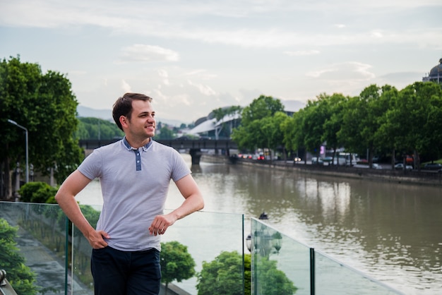 Foto van de Jonge Mens die dichtbij de rivier bij Europese groene stad blijft. Knappe jongen Outdoor portret