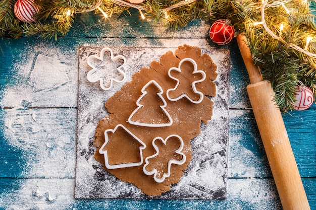 Foto van dennentakken, deeg, koekjesvormen, deegroller op blauwe houten tafel