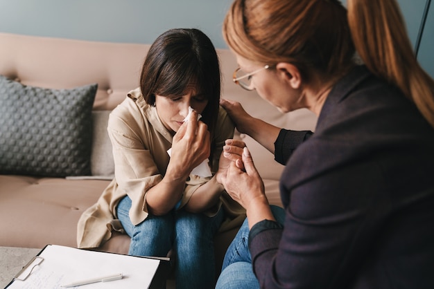 Foto van depressieve blanke vrouw die huilt en een gesprek heeft met psycholoog tijdens therapiesessie in de kamer