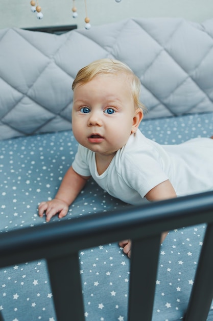 Foto van een 5 maanden oude baby die in een wieg ligt Een wieg met een kleine jongen in een wit bodysuit