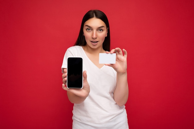 Foto van een aantrekkelijke, gelukkige jonge brunette vrouw die een casual wit t-shirt draagt dat over rood wordt geïsoleerd