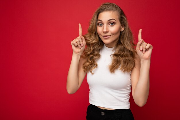 Foto van een aantrekkelijke positieve jonge vrouw die met de vingers omhoog wijst naar copyspace die advertenties promo presenteert met oprechte emoties die een goed uitziende outfit dragen, geïsoleerd op de achtergrond met vrije ruimte.